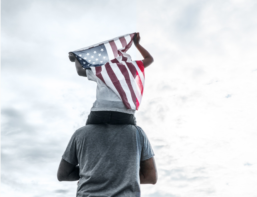 Image of a boy holding USA flag while riding on father's shoulders